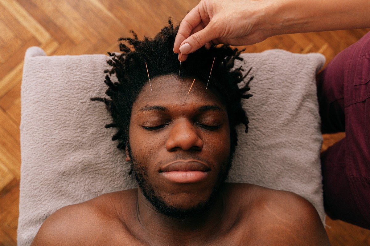 A man receiving acupressure treatment, lying down with eyes closed, therapist applying pressure on specific points.